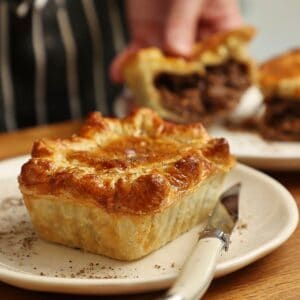 South African pepper steak pie on a white plate with a cross section of a pie cut in half in the background.