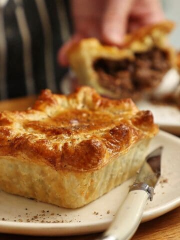 South African pepper steak pie on a white plate with a cross section of a pie cut in half in the background.