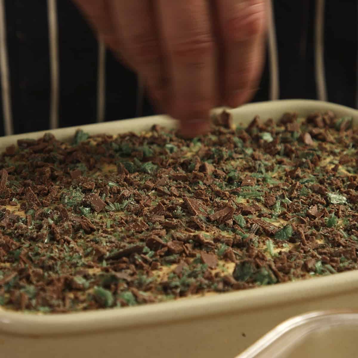 Sprinkling chopped chocolate over cream dessert in a green dish.