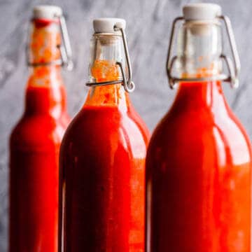 Sriracha hot sauce in swing top bottles on a grey background.