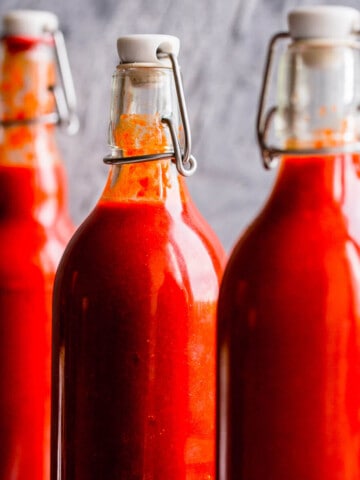 Sriracha hot sauce in swing top bottles on a grey background.
