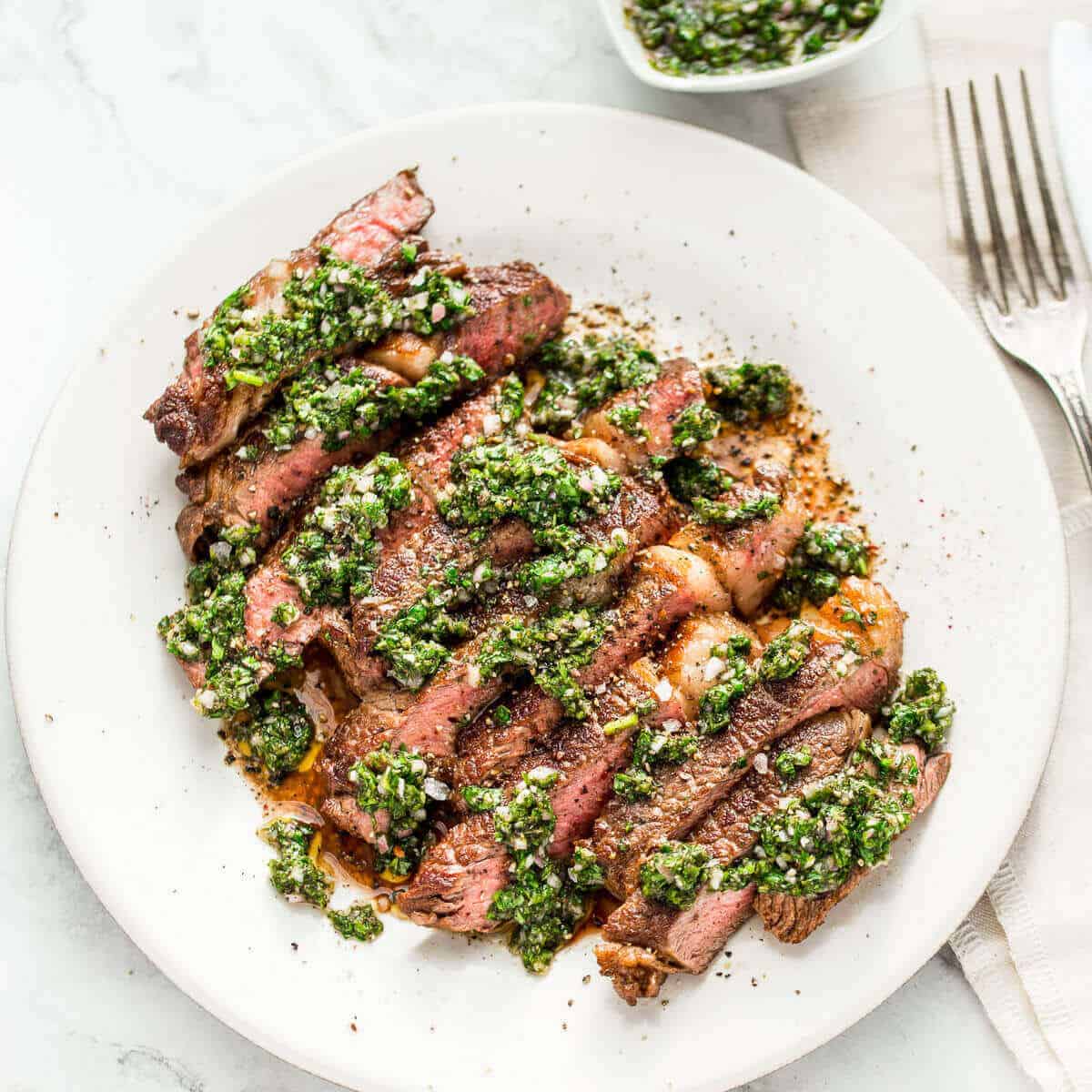 sliced steak with chimichurri sauce on white plate