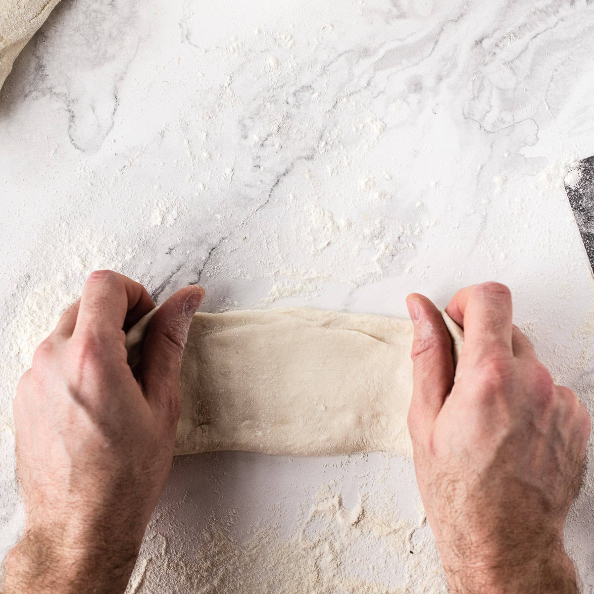 Shaping sourdough baguettes by hand on a marble surface. Flattening the dough.