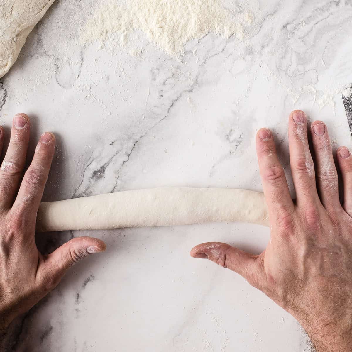 Rolling baguettes into shape with two hands.