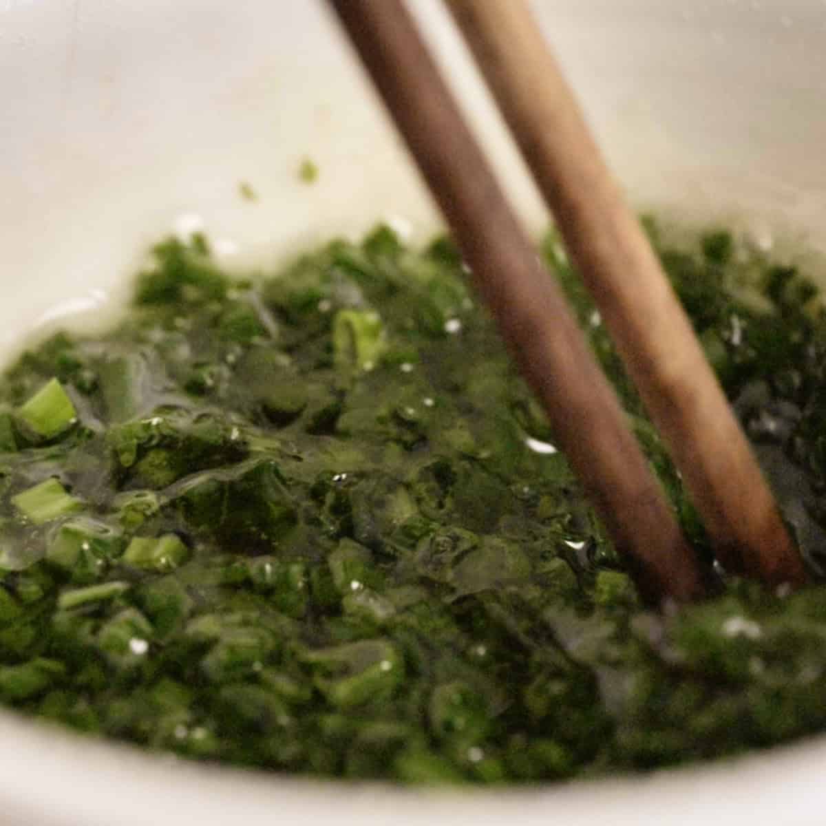 Stirring hot oil into chopped scallions with chop sticks.