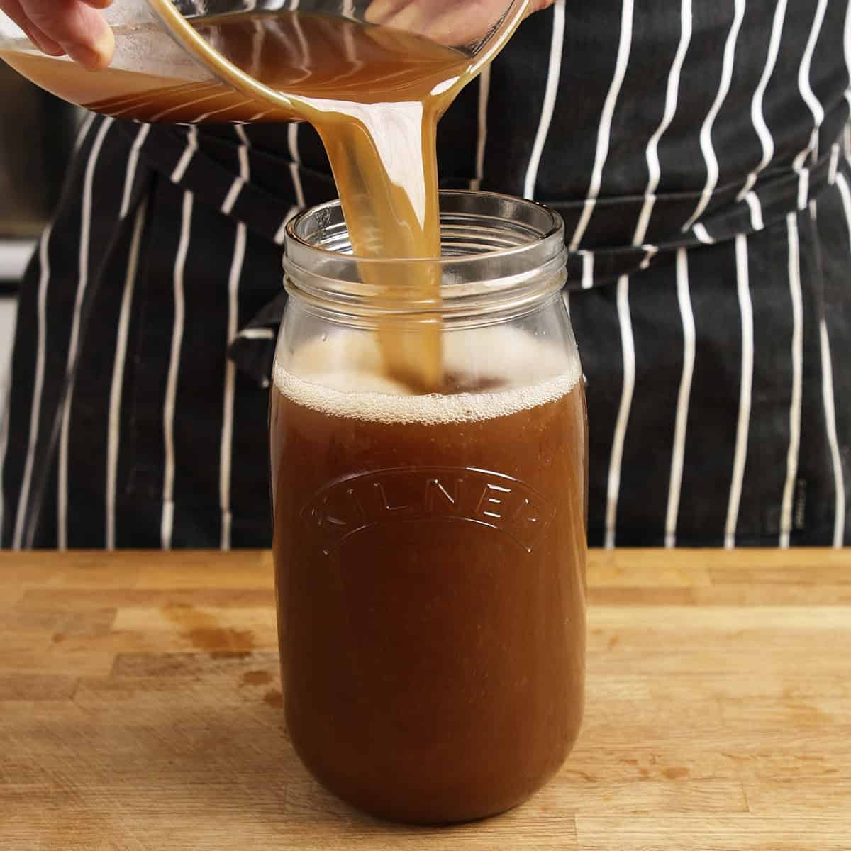 Pouring fresh beef stock into a glas jar for storage.