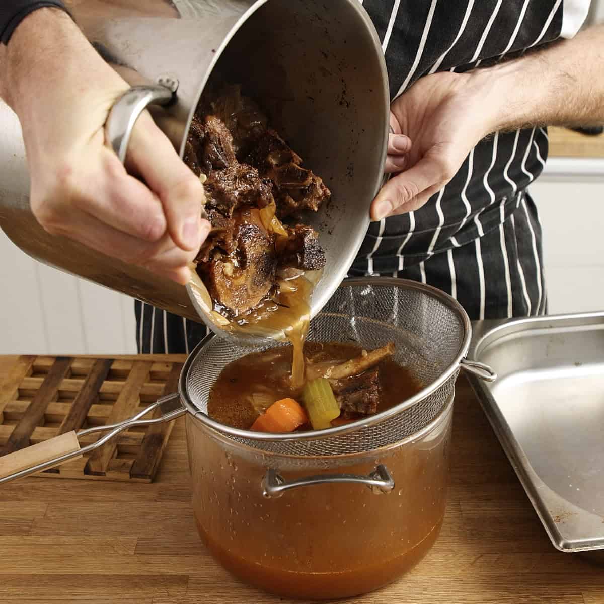 Straining beef stock through a fine mesh sieve.
