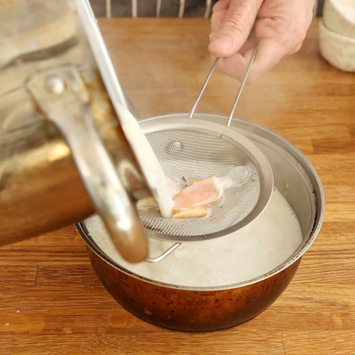 Straining infused milk mixture through fine-mesh sieve into a pot.