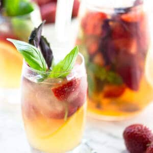 Strawberry lemonade in glass and jug on marble background.