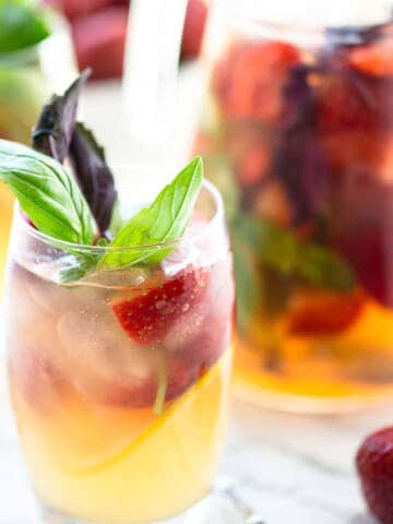 Strawberry lemonade in glass and jug on marble background.