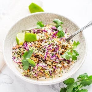 Coleslaw with cilantro and lime in a white bowl on marble background.