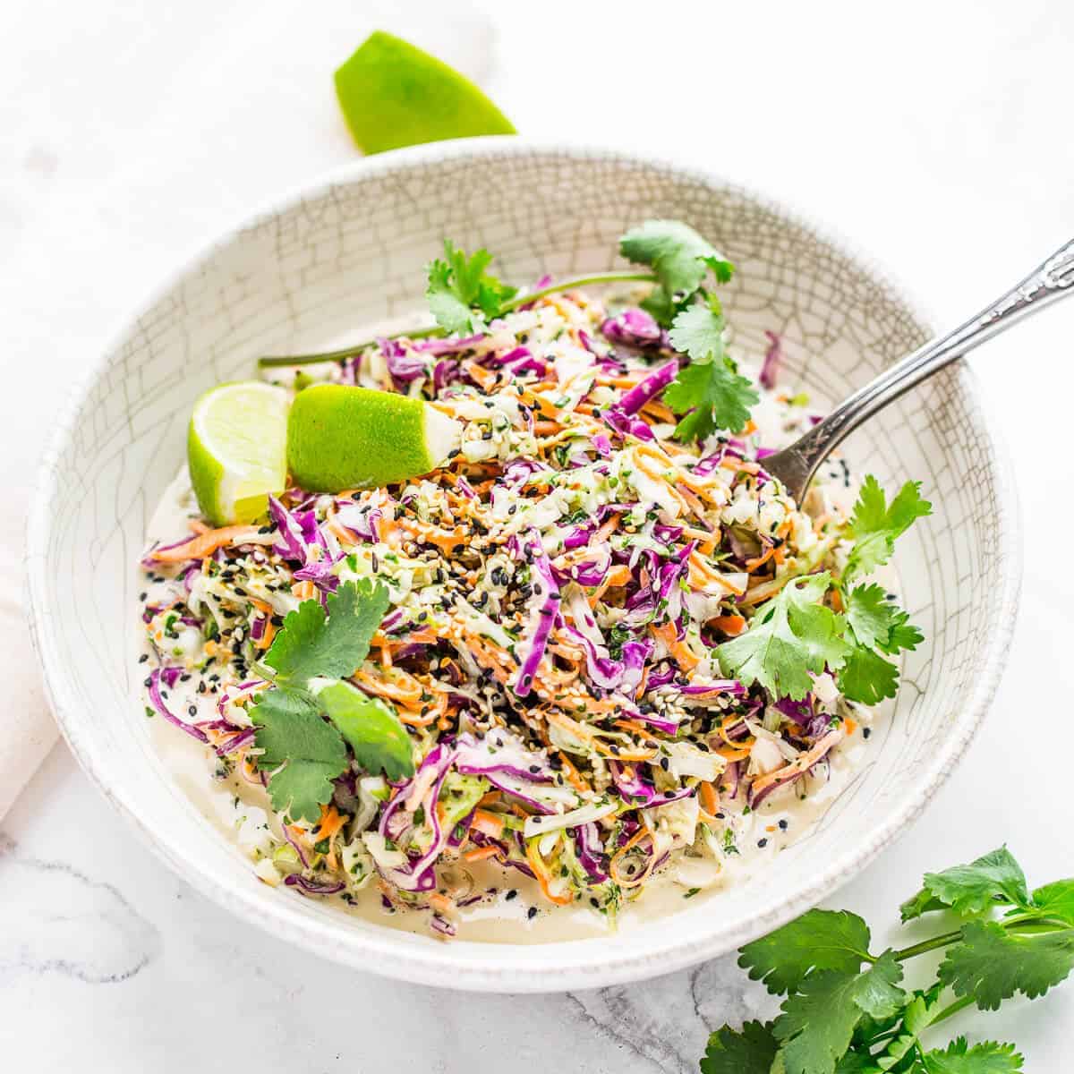 coleslaw with cilantro and lime in a white bowl on marble background.