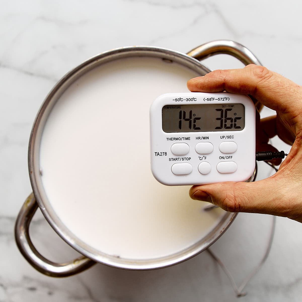 Kitchen thermometer showing the temperature of milk in a pot.