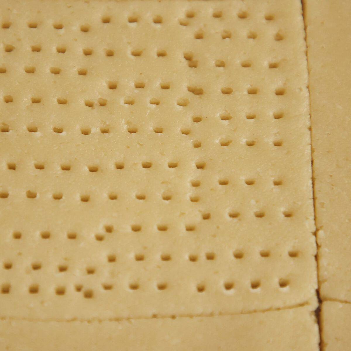 Tennis biscuit dough cut into 8cm squares and docked all over with a fork, showing characteristic pattern