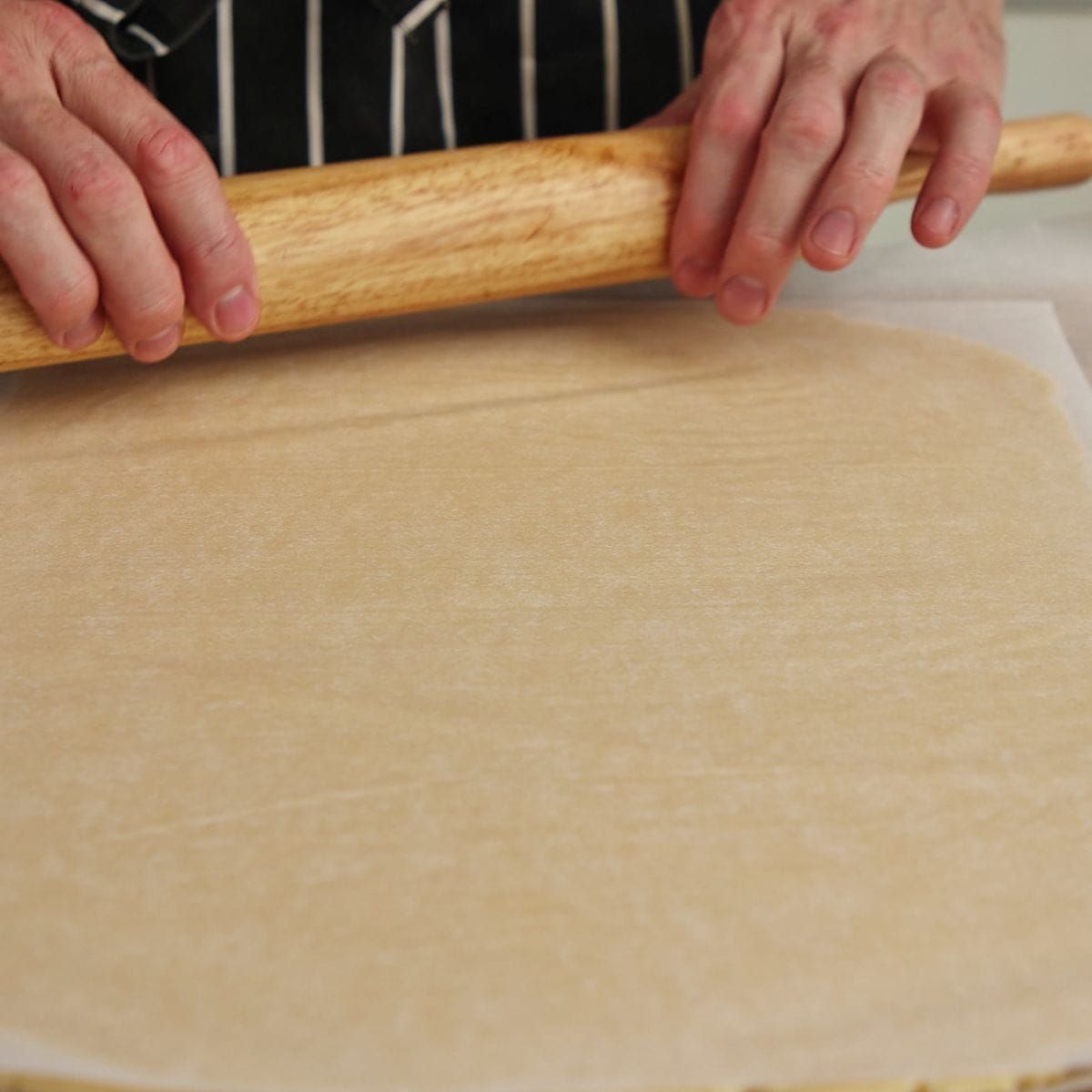 Tennis biscuit dough rolled out between two sheets of parchment paper to 3-4mm thickness