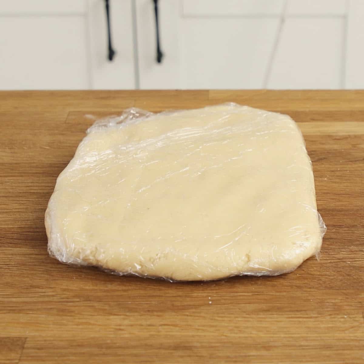 Biscuit dough wrapped in plastic on wooden table.