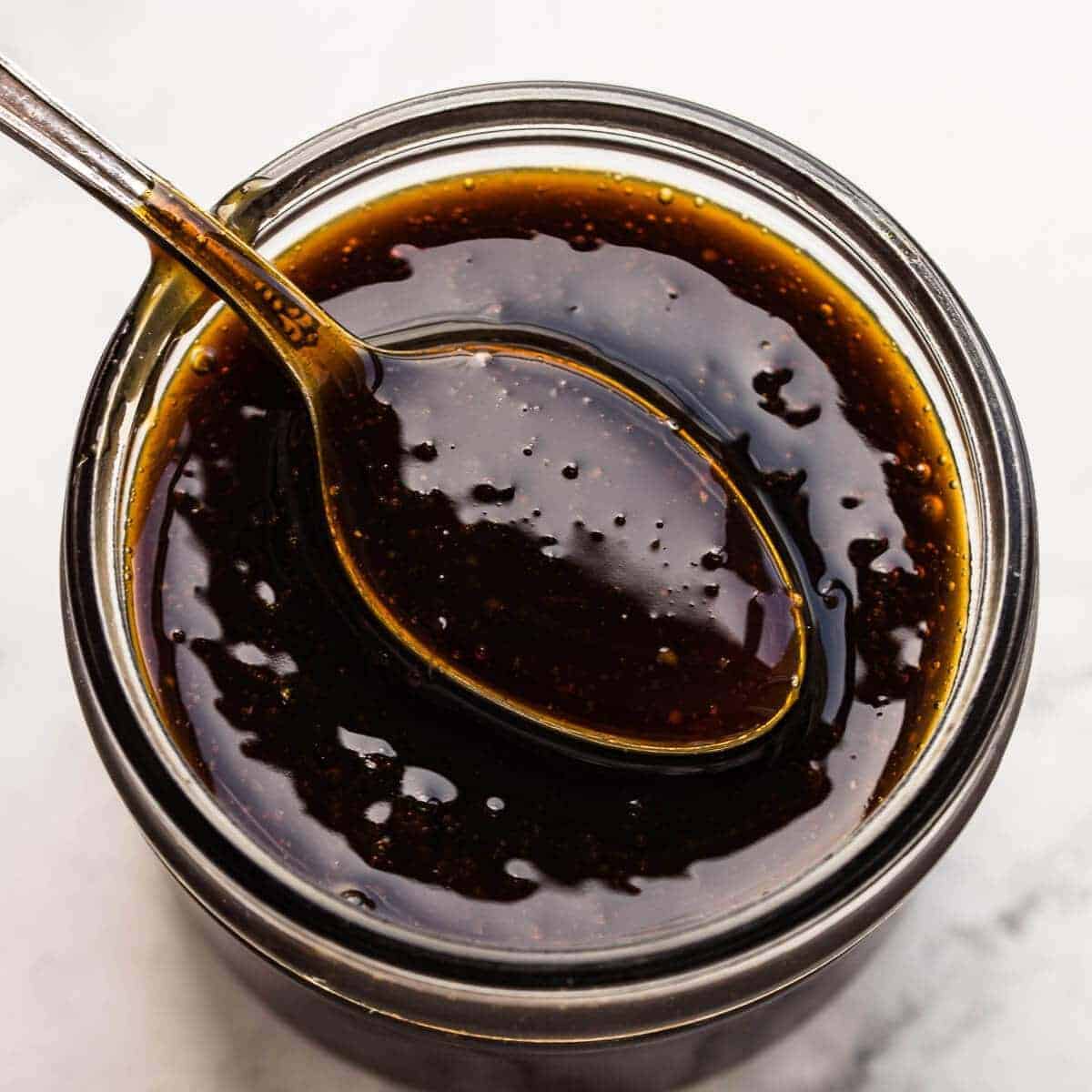 Spoon of homemade teriyaki sauce in a jar on marble background.