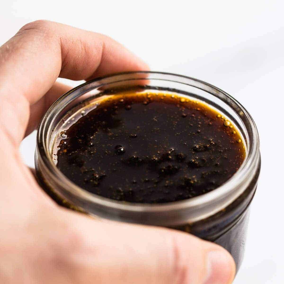 Teriyaki sauce in a glass jar held by a hand.