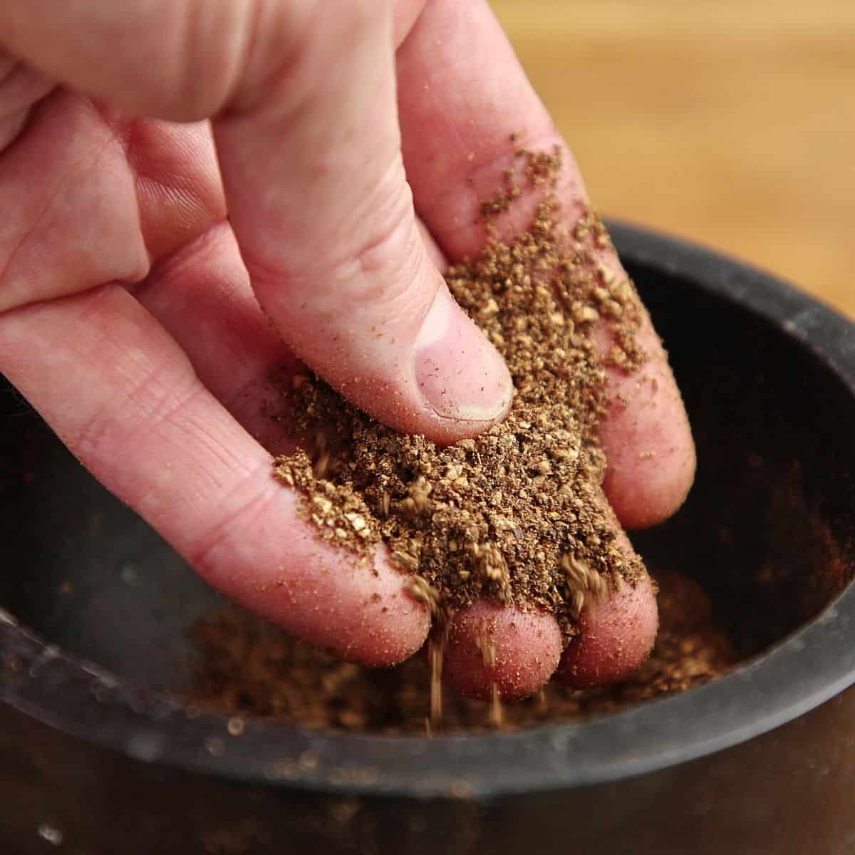 Toasted spices being crushed with mortar and pestle showing coarse cracked texture, not powder