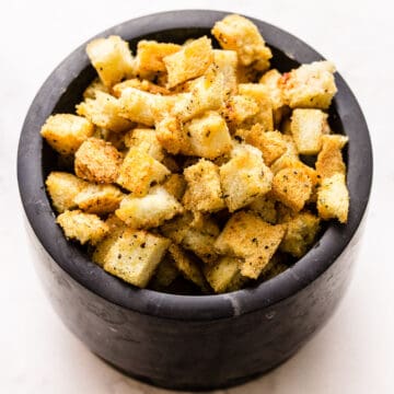 homemade croutons in a black bowl on white background.