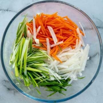 Scallions, carrot, and daikon strips in a glass bowl.