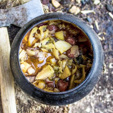 viking stew in a black cauldron on a wood log next to and old axe