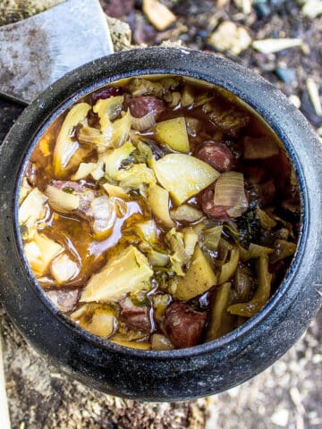 viking stew in a black cauldron on a wood log next to and old axe