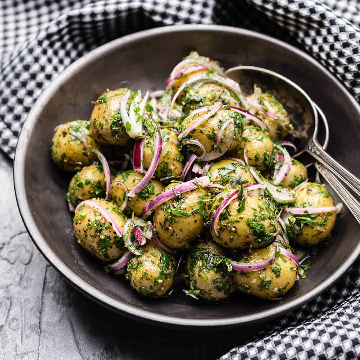 warm potato salad with red onion and parsley in a black bowl with black and white checkered napkin