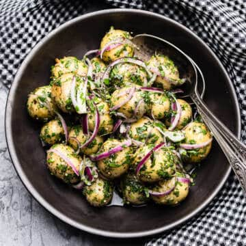 warm potato salad with red onion and parsley in a black bowl with black and white checkered napkin