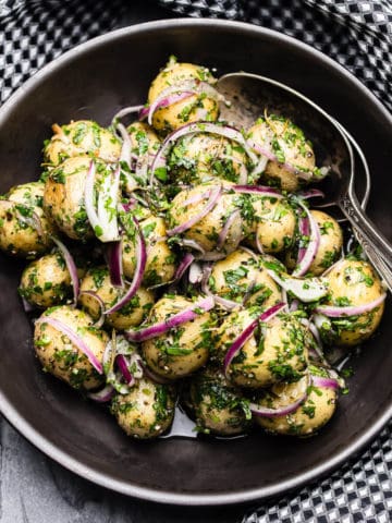 warm potato salad with red onion and parsley in a black bowl with black and white checkered napkin
