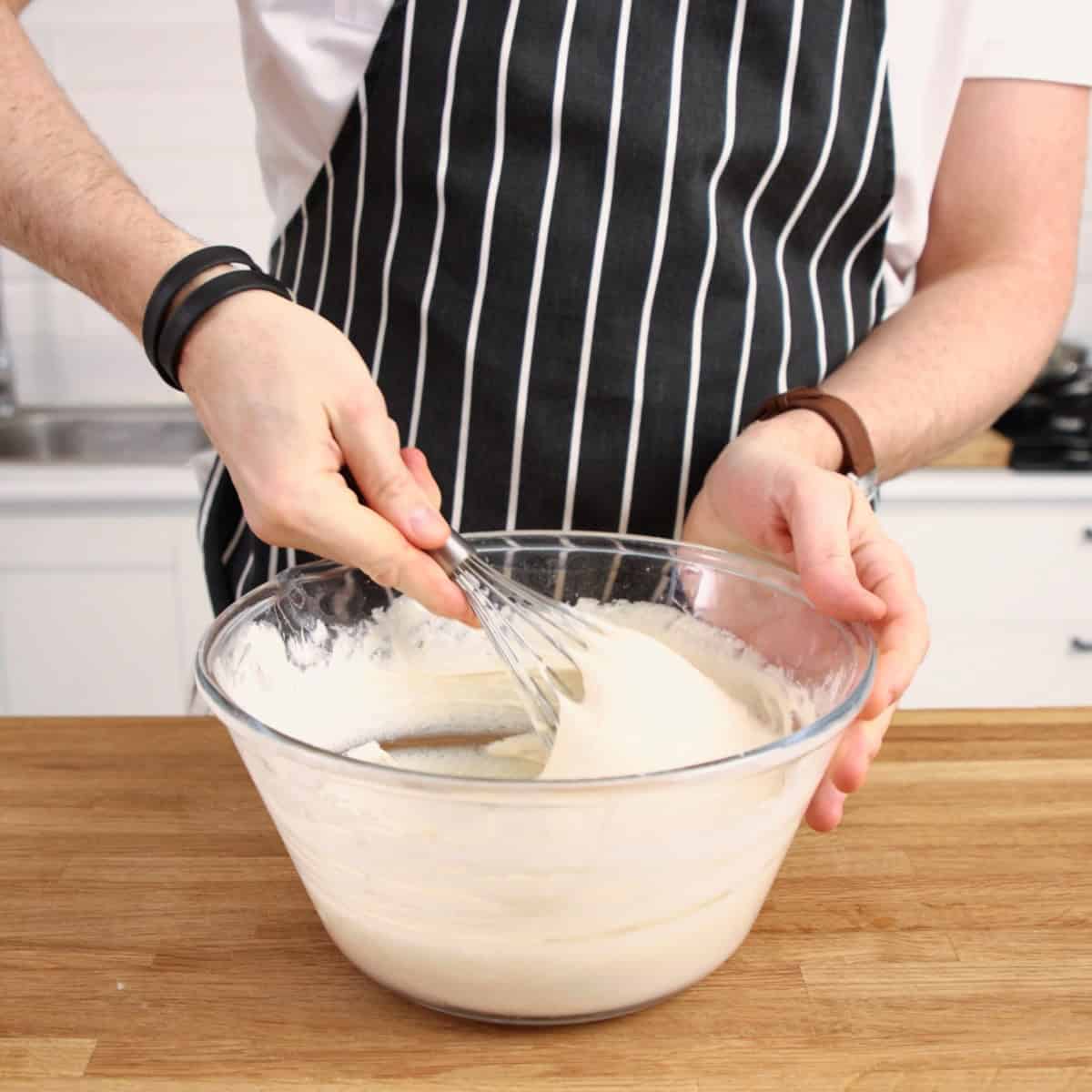 Whisking crumpet batter in glass bowl.