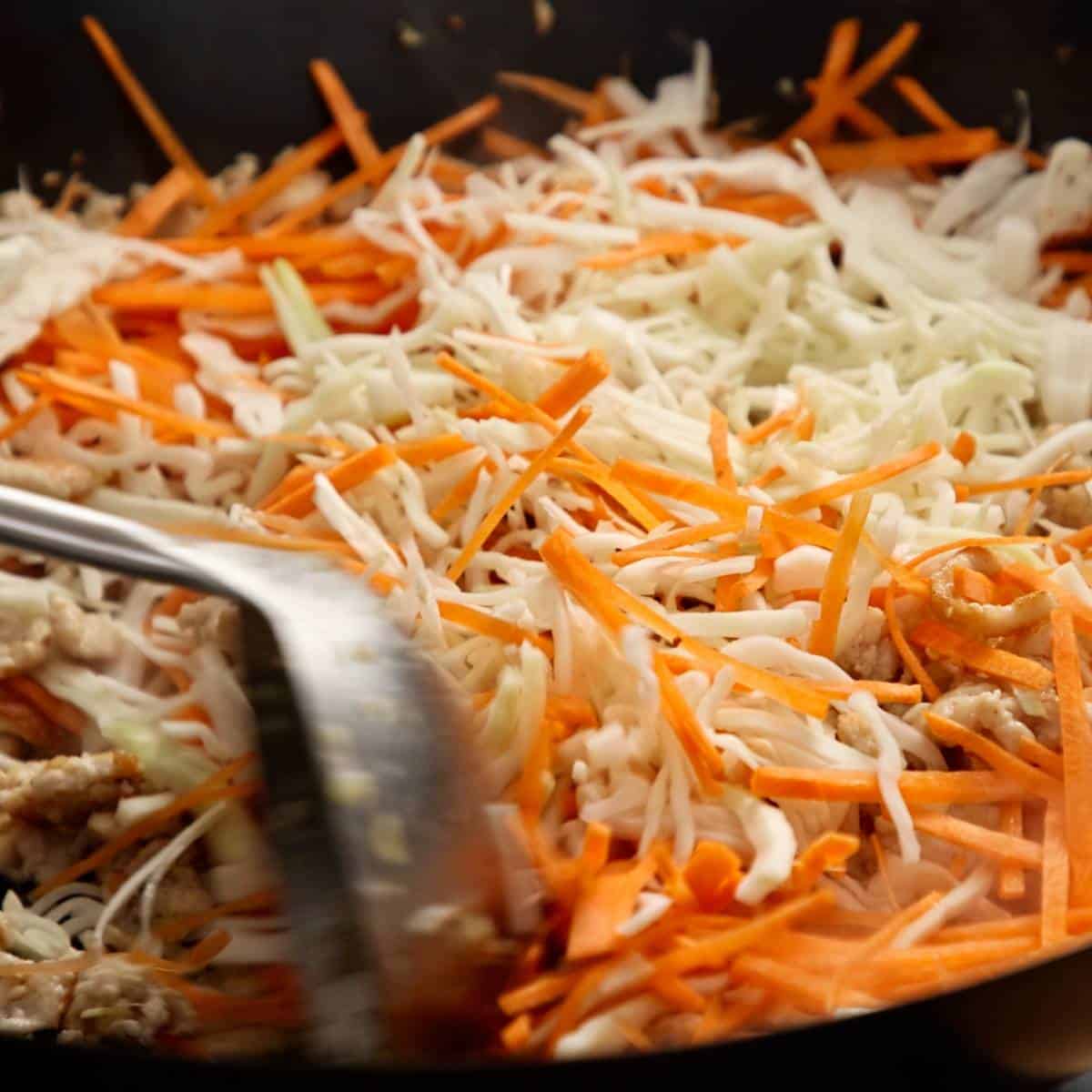 Wok frying finely sliced vegetables for spring roll filling.